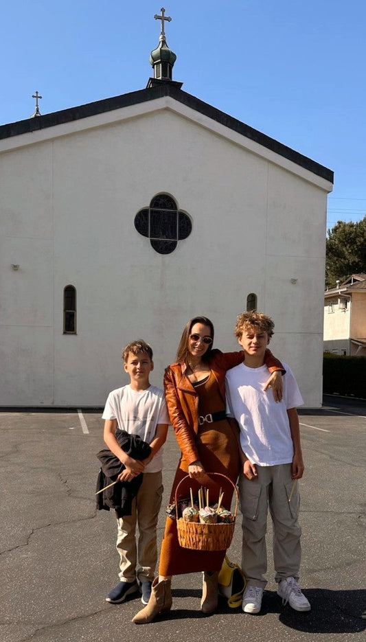 Alyona and her two sons standing in front of a white chapel on Easter Sunday, dressed in spring outfits